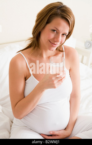 Pregnant woman sitting in bedroom with glass of water smiling Stock Photo
