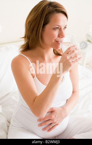 Pregnant woman sitting in bedroom with glass of water smiling Stock Photo