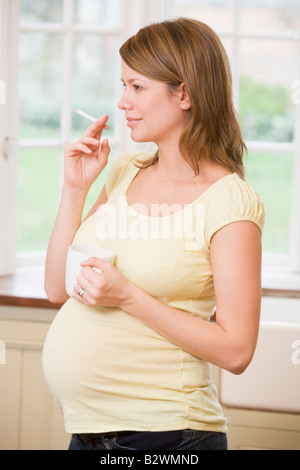 Pregnant woman standing in kitchen with coffee and cigarette Stock Photo