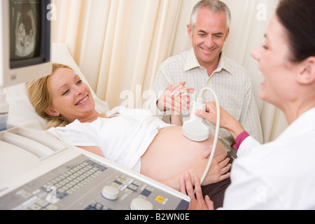 Pregnant woman getting ultrasound from doctor with husband watching Stock Photo