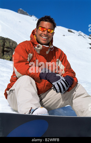 Snowboarder sitting on hill with board smiling (selective focus) Stock Photo