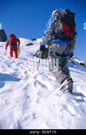 Two mountain climbers walking up snowy mountain (selective focus) Stock Photo