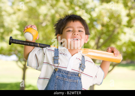 Young boy holding baseball bat outdoors smiling Stock Photo