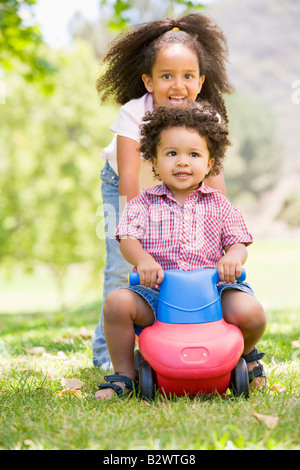 Sister pushing brother on toy with wheels smiling Stock Photo