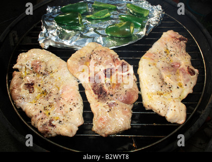 Raw pork chops and jalapeño peppers grilling on a barbecue. Stock Photo