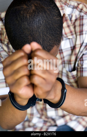 A young black male in handcuffs. Shot with minimum depth of field Focus is on the cuffs. Stock Photo