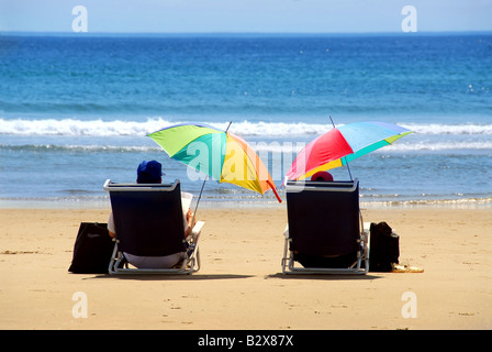 A couple relaxing on a beach under colorful umbrellas Stock Photo