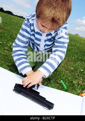 Young boy draws a picture of his toy gun in the park on a sunny day Small boy painting in the park on a summers day in Kent Engl Stock Photo