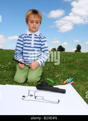 Young boy draws a picture of his toy gun in the park on a sunny day Small boy painting in the park on a summers day in Kent Engl Stock Photo