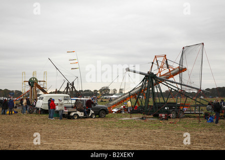 Assortment of catapults and human powered machines line the side of competition field along with support vehicles and owners Stock Photo