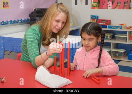 Caucasian preschool teacher helping her 4 year old Filipino girl student stacking blocks Stock Photo