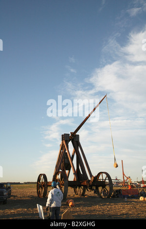 Huge iron wheeled Yankee Siege Trebuchet with fling arm rising towards vertical and pumpkin in sling rising behind it Stock Photo