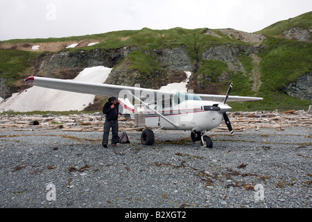 Pilot inspecting his airplane before taking of from a beach covered with driftwood in Katmai, Alaska Stock Photo