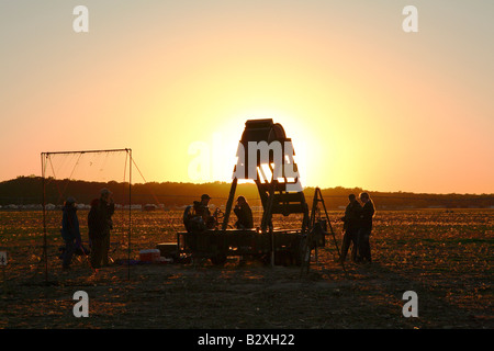 Wooden barrel shaped human powered pumpkin flinging machine with glow of setting sun directly behind Stock Photo