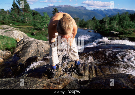 Woman outdoors by river splashing water on face (selective focus) Stock Photo