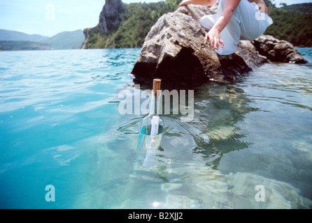 Woman outdoors reaching into ocean for bottle with note inside (selective focus) Stock Photo