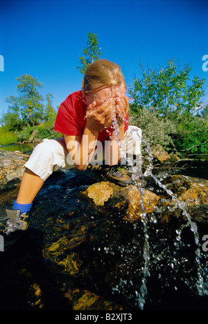 Woman outdoors by a lake splashing water on face Stock Photo