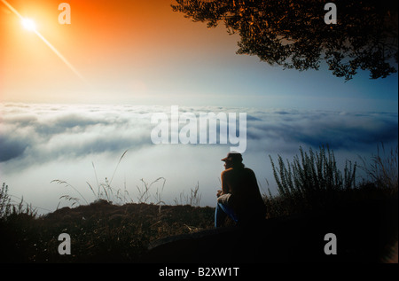 Man sitting alone on mountain top in Laguna Beach, California at sunrise Stock Photo