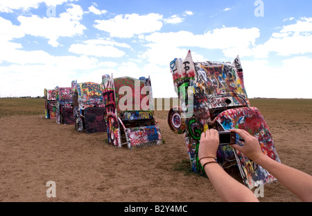 Tourist taking picture with camera at the Cadillac Ranch with buried cars in ground in Amarillo Texas USA Stock Photo