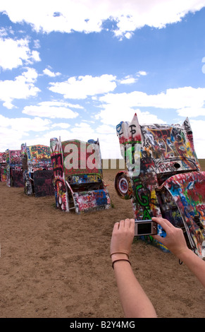 Tourist taking picture with camera at the Cadillac Ranch with buried cars in ground in Amarillo Texas USA Stock Photo