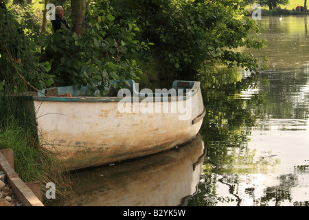 An old fibreglass dinghy tied up at the edge of a fishing lake Stock Photo