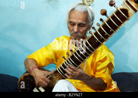 A colorful Indian sitar player sits and plays a melody against a wall. Stock Photo