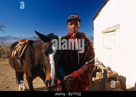 Man wrapped in basotho blanket with his horse outside village building, portrait, Lesotho, Africa Stock Photo