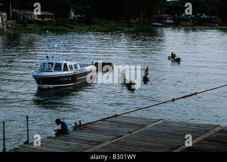 Scene on lake with police patrol boat, row boats and boy fishing on pier. Malawi. Mozambique. Stock Photo