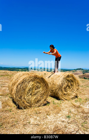 Middle aged woman depicting freedom by standing on rolls of hay in farm field during the summer time in Tuscany Italy Stock Photo