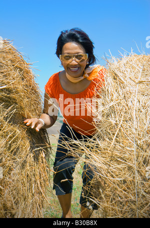 Woman looking between two hay rolls enjoying herself in the fields, Tuscany, Italy Stock Photo