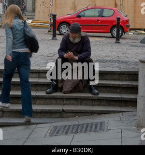 A haggard, bearded guy sitting on the streets of London, trying to warm his hands Stock Photo