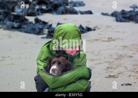 A young woman cuddling a wet dog on a beach on a rainy day Stock Photo