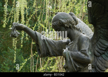 angel sculpture seen from the side holding a rose flower in its raised right hand Stock Photo