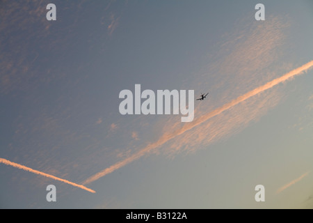 Jet airliner banks against some contrails that have turned pink as the sun sets Stock Photo