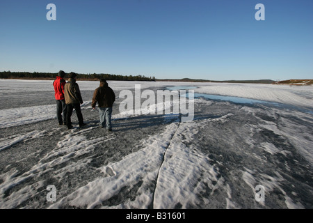 Three men walking on a frozen lake with huge cracks and melting ice. Stock Photo