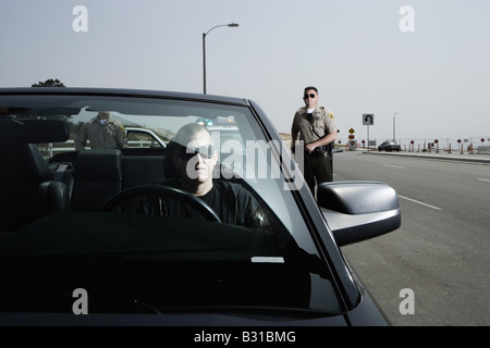 Two police officers approaching man in black Mustang Stock Photo