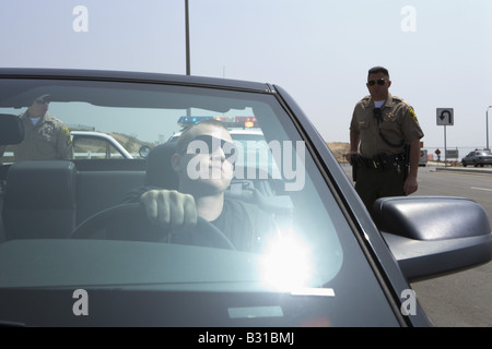 Two police officers approaching man in black Mustang Stock Photo