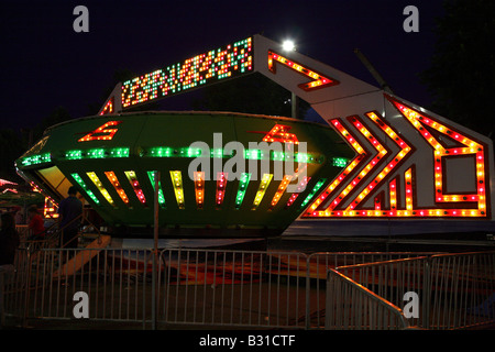 Space ship funfair ride.  Large flying saucer shape with bands of multi colored lights on the outside of fancy geometric shape. Stock Photo