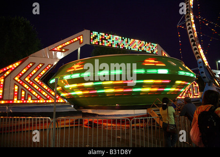 Space ship funfair ride.   Large flying saucer shape whorling around with three vertical bands of multi colored lights Stock Photo