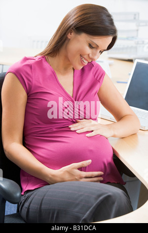 Pregnant woman at work holding belly and smiling Stock Photo