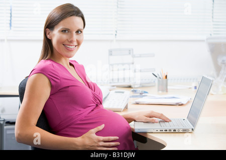 Pregnant woman at work using laptop and smiling Stock Photo