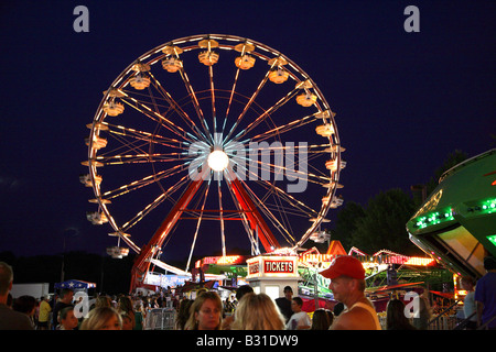 The Big Wheel or funfair Ferris wheel all lit up at night from across fairgrounds Stock Photo