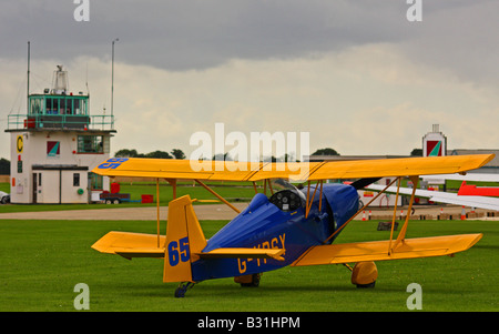 A blue and yellow Andreasson bi-plane with a control tower in the background Stock Photo
