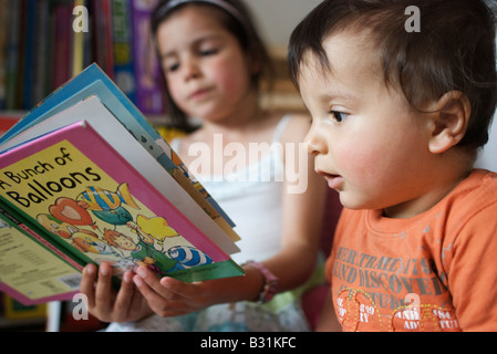 Older sister reads a story to her baby brother Stock Photo