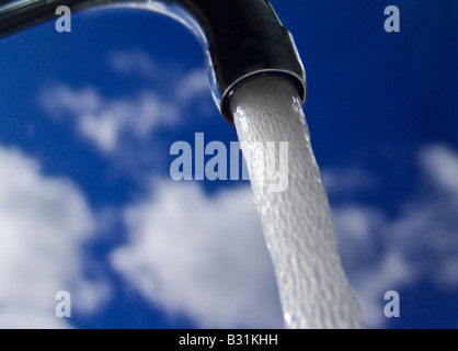 TAP RUNNING WATER BLUE SKY Dramatic low angle view of running water from a domestic tap against bright blue sunny sky and clouds Stock Photo