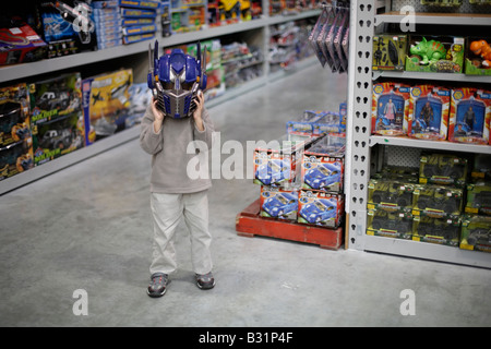 Six year old boy in toystore tries on Optimus Prime robot helmet from the Spielberg movie Transformers Stock Photo