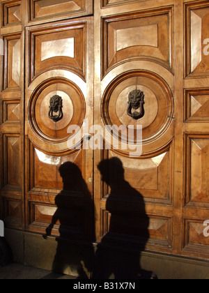 Two women walk past a carved red sandstone arch with floral and ...