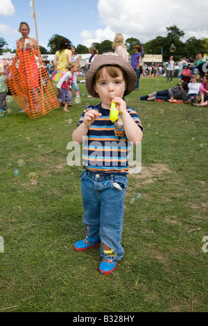 Boy blowing bubbles through a toy bubble-pipe in the sunshine at the Big Chill festival 2008 Stock Photo