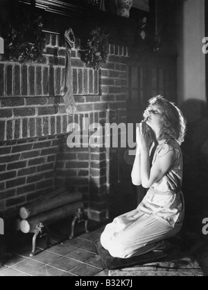 Portrait of teenage girl praying at hearth with Christmas stocking Stock Photo