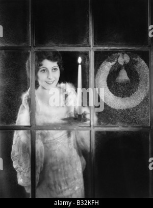 Woman with candle and Christmas wreath in window Stock Photo